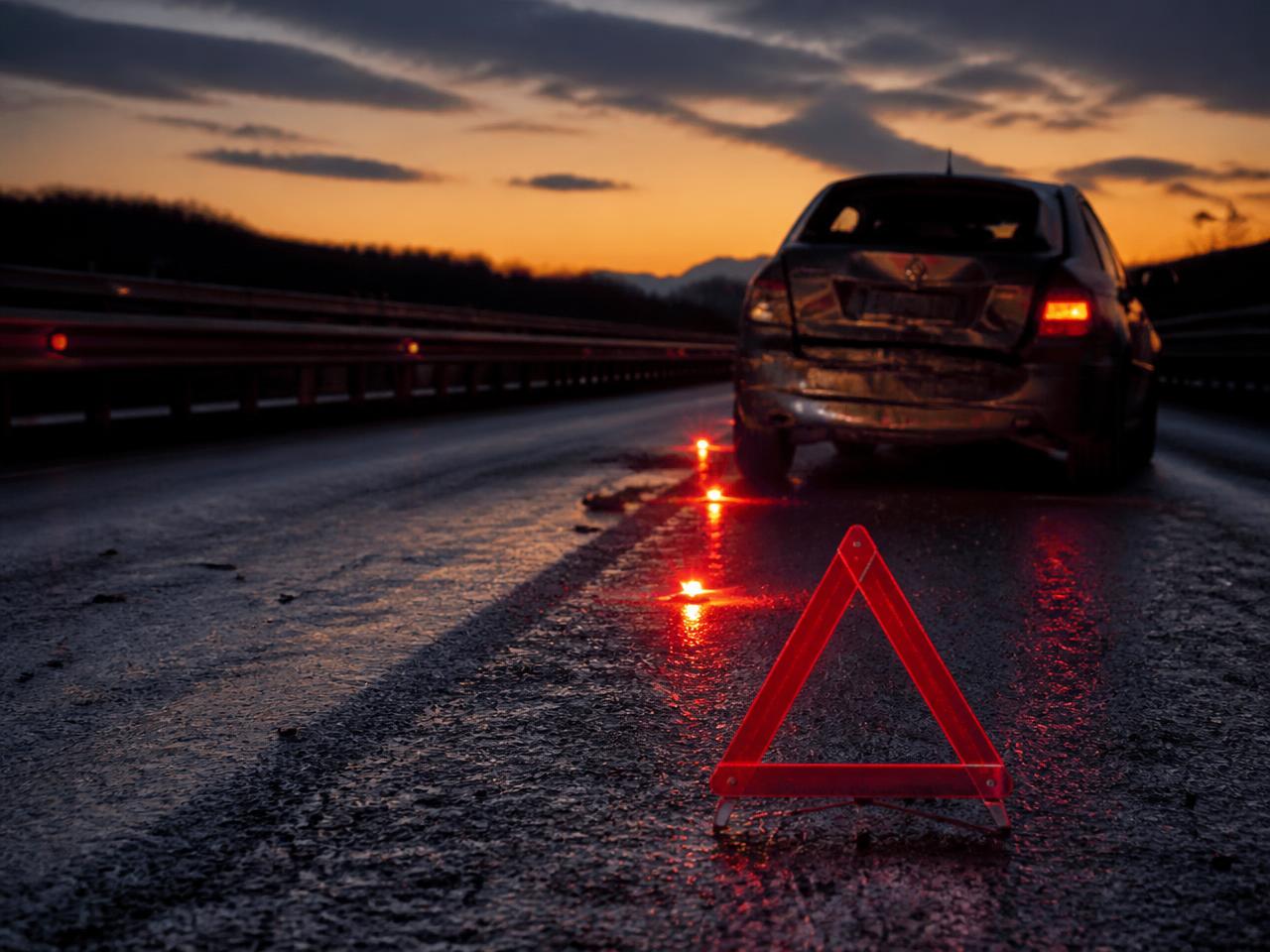 Damaged car on a highway shoulder with a reflective warning triangle at dusk
